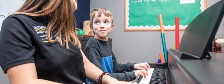 A music therapy student plays piano with a young student.